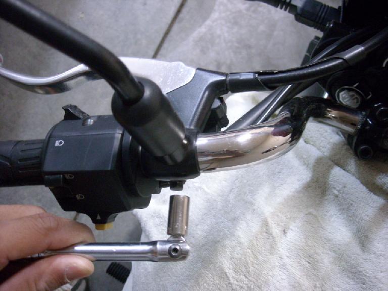 Using a metric hex socket to remove the assembly for the clutch lever and left mirror from the handlebars. Using a metric hex socket to remove the assembly for the clutch lever and left mirror from the handlebars.