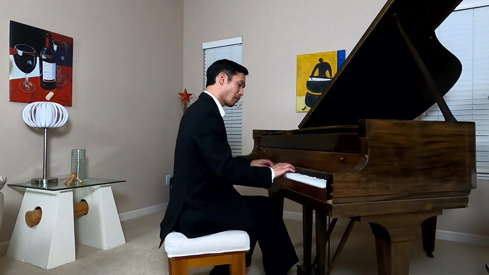 Felix Wong wearing a black suit playing a baby grand piano in his livng room