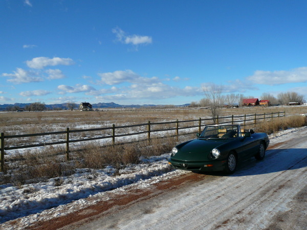 green 1991 Alfa Romeo spider with top down on snow-covered dirt road