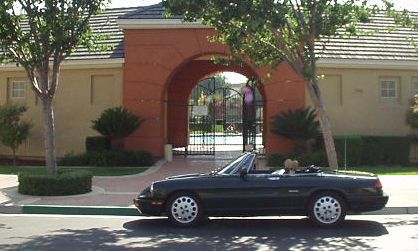 green 1991 Alfa Romeo Spider with top down in front of orange archway of HOA pool