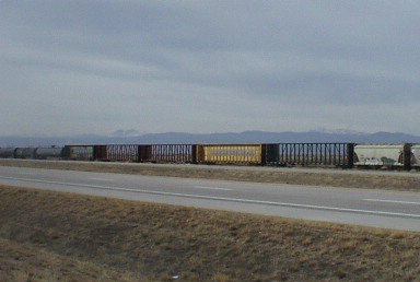 train with Interstate I-25 in the foreground and the Front Range foothills in the background