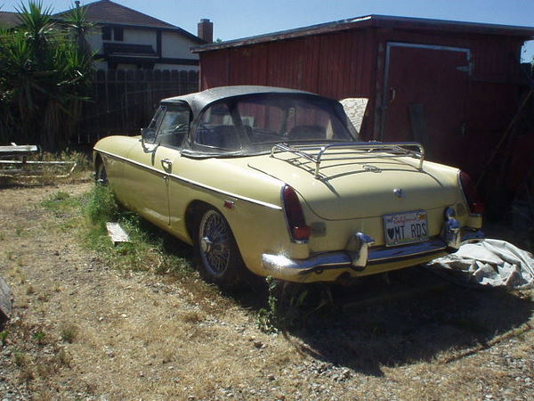 yellow 1969 MGB with top up next to wooden shack