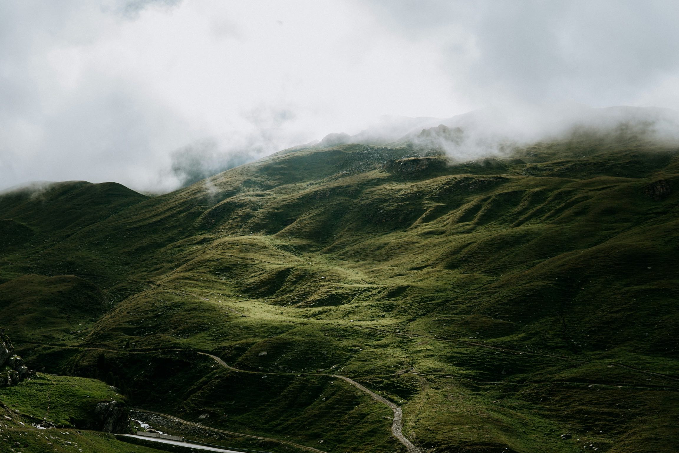 green mountain with windy road enshrouded by clouds