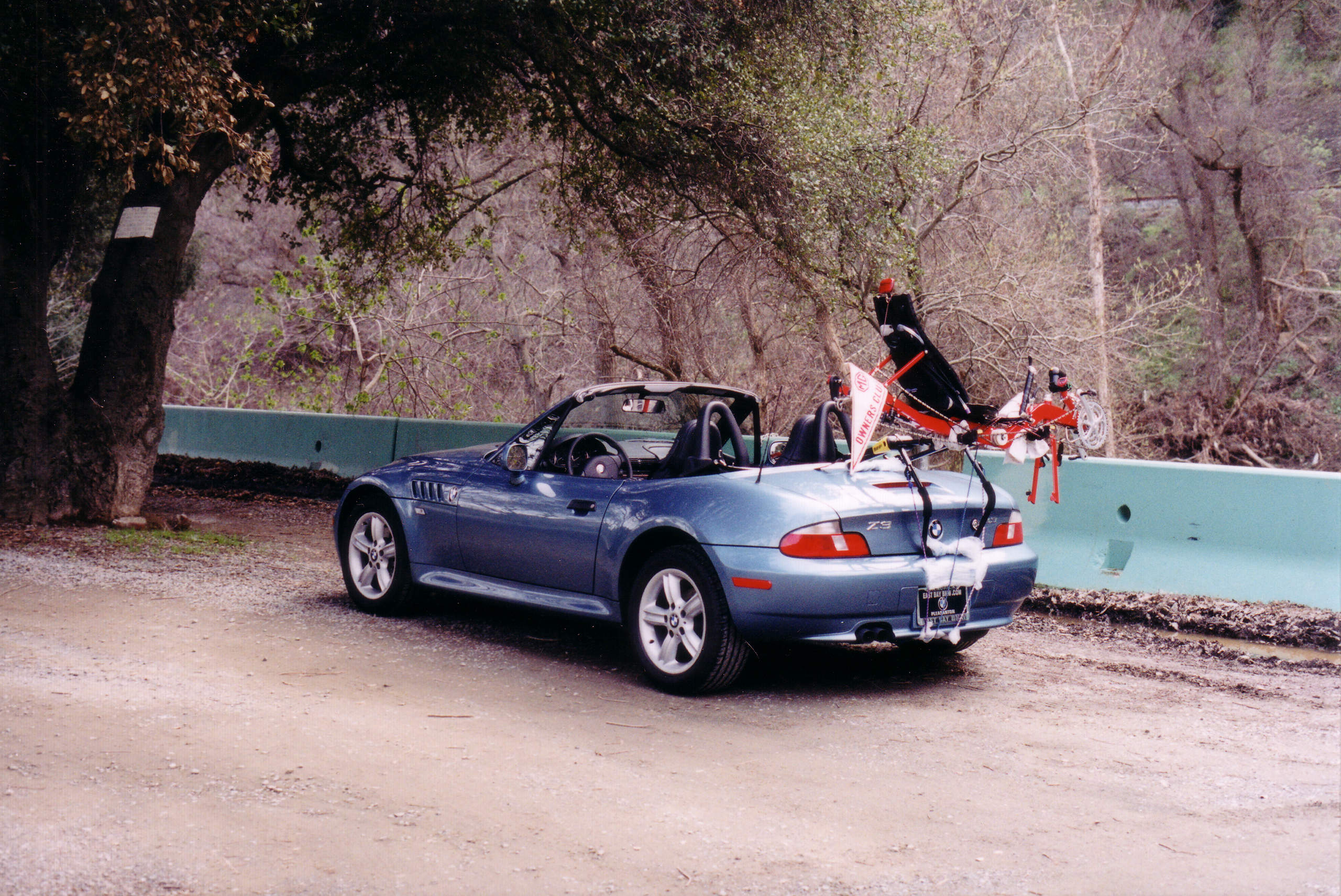 Atlanta Metallic Blue 2003 BMW Z3 Rodaster with top down and red recumbent without wheels on bike rack on the trunklid, MGOC banner on recumbent frame