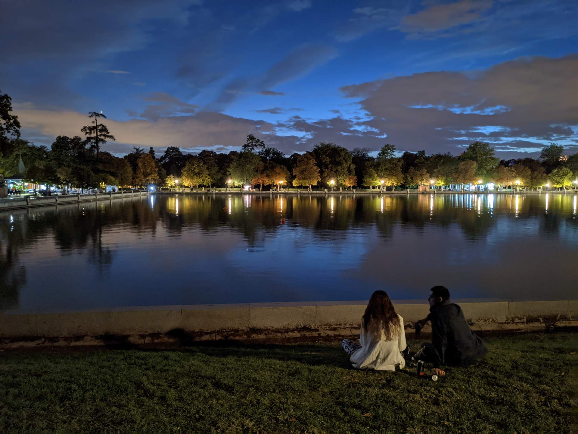A girl and a guy sitting alone in front of the lake at Parque del Retiro in Madrid.