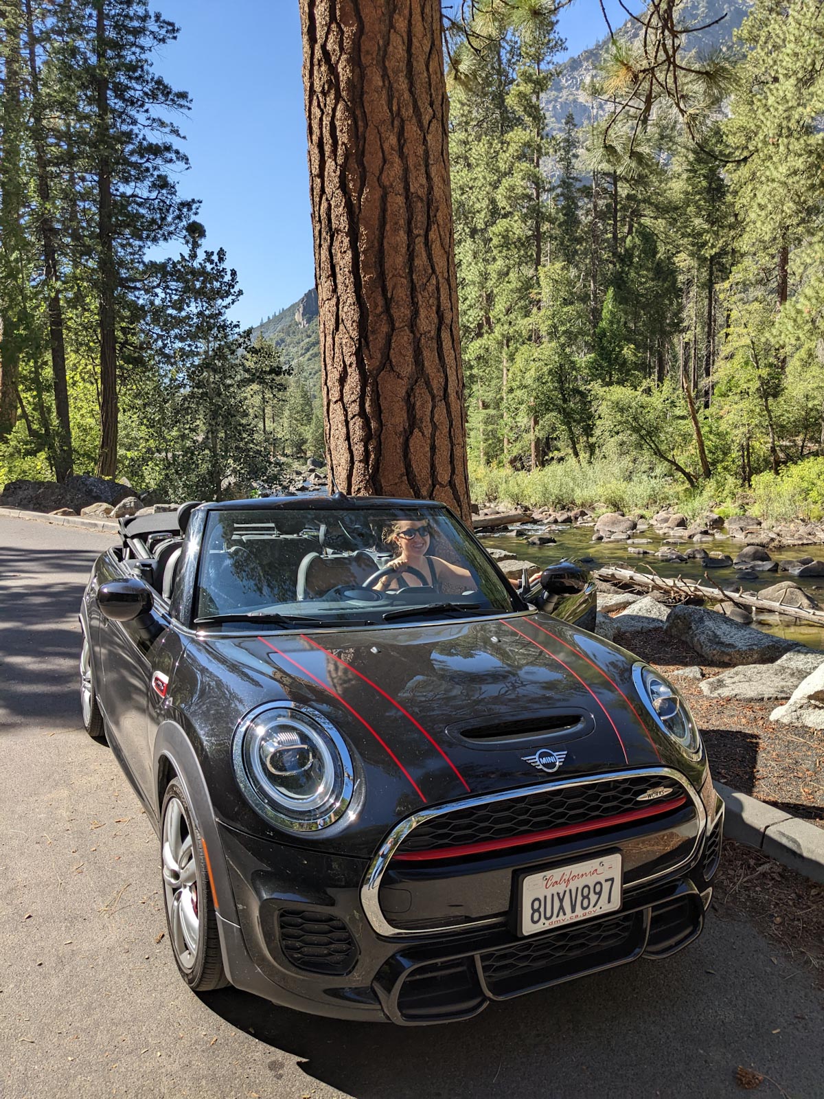 Andrea in the black MINI Convertible with red pinstripes by the Merced River in Yosemite.