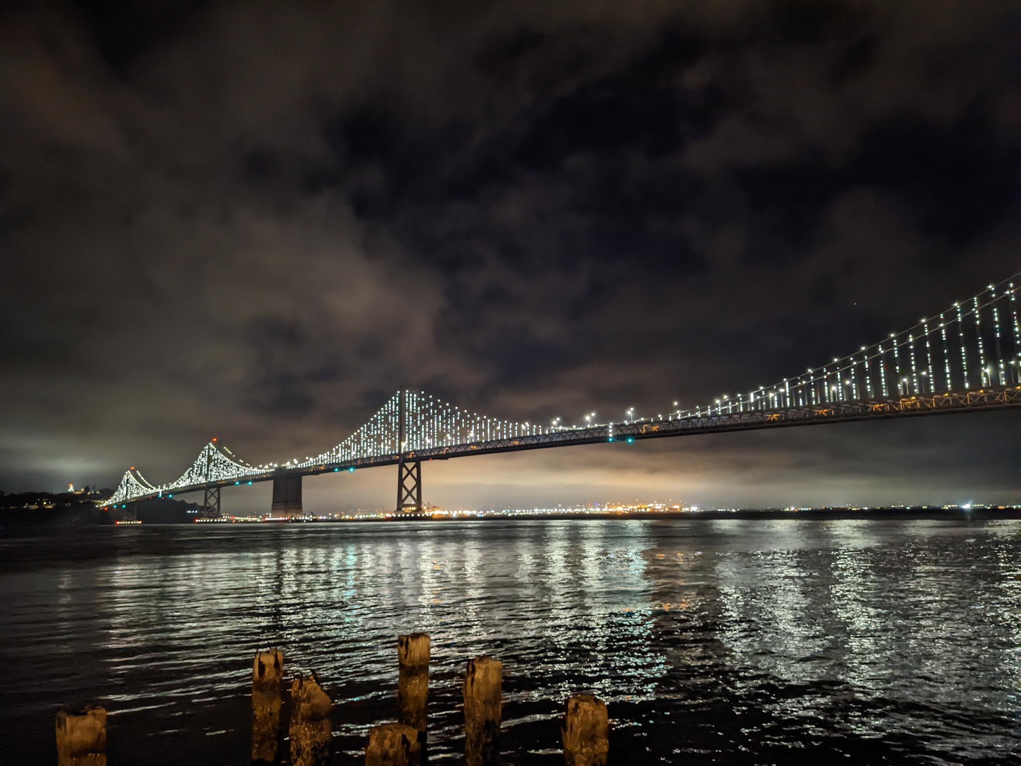 The Bay Bridge at night as viewed from the Embarcadero in San Francisco. You can also see the lights from Oakland in the distant background.