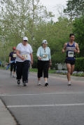 Felix Wong in a blue and white singlet running past two female walkers