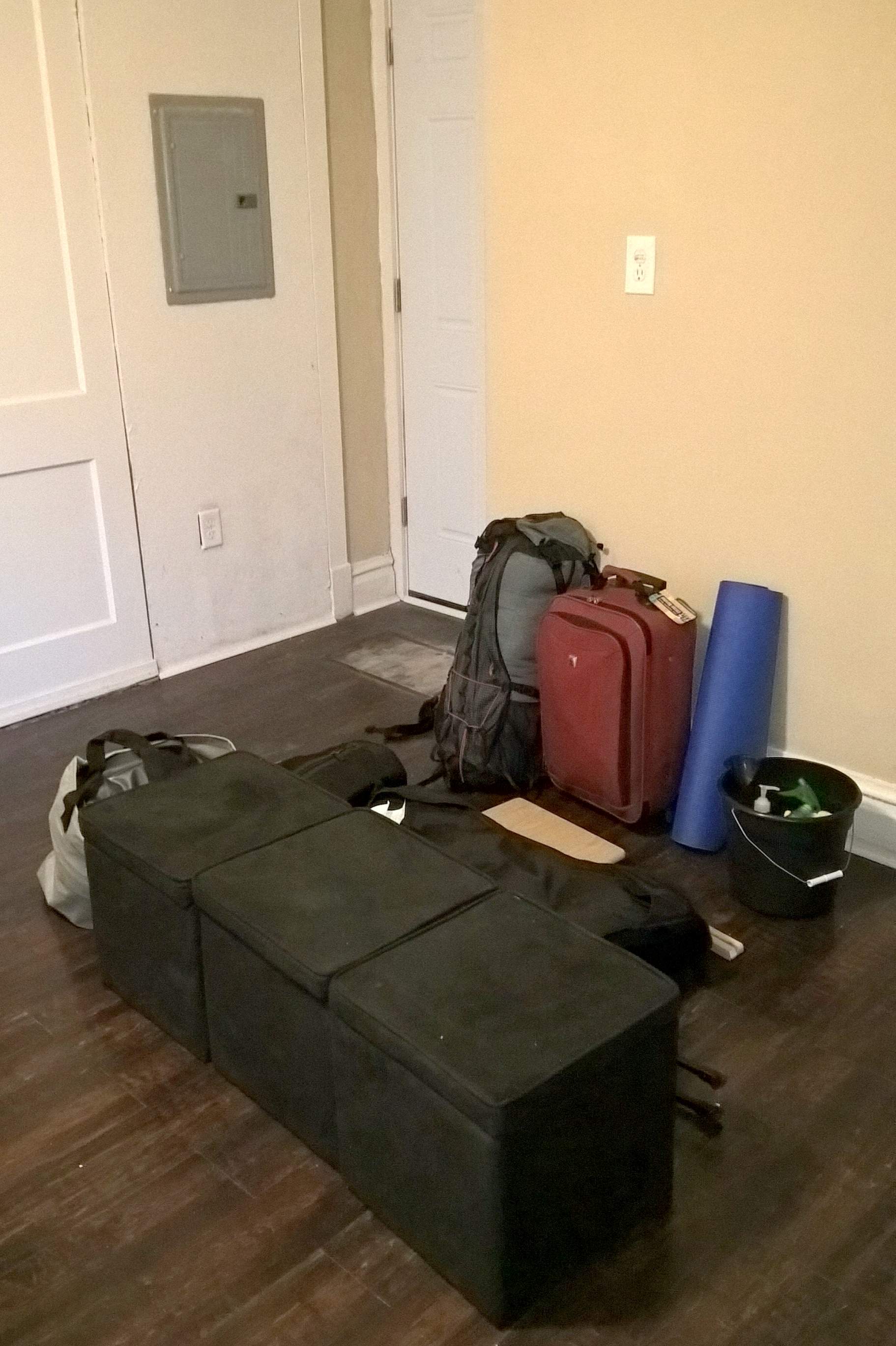 backpack, red suitcase, blue yoga mat, bucket, three black ottomans 