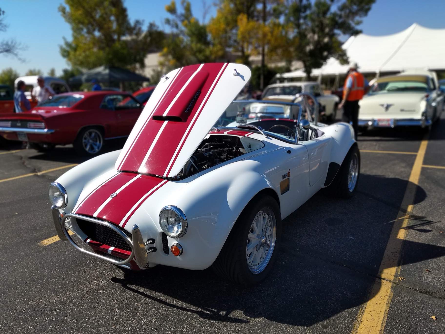 A white AC Cobra replica with red racing stripes.