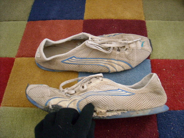 gloved hand in two-inch-long tear on left side of left Puma H-Street shoe, right shoe in background on colorful doormat