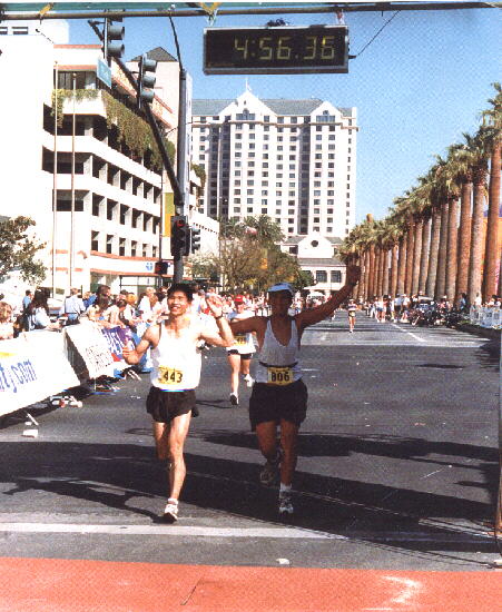 Felix Wong and Dan Lieb crossing a finish line underneath a clock reading 4:56:36