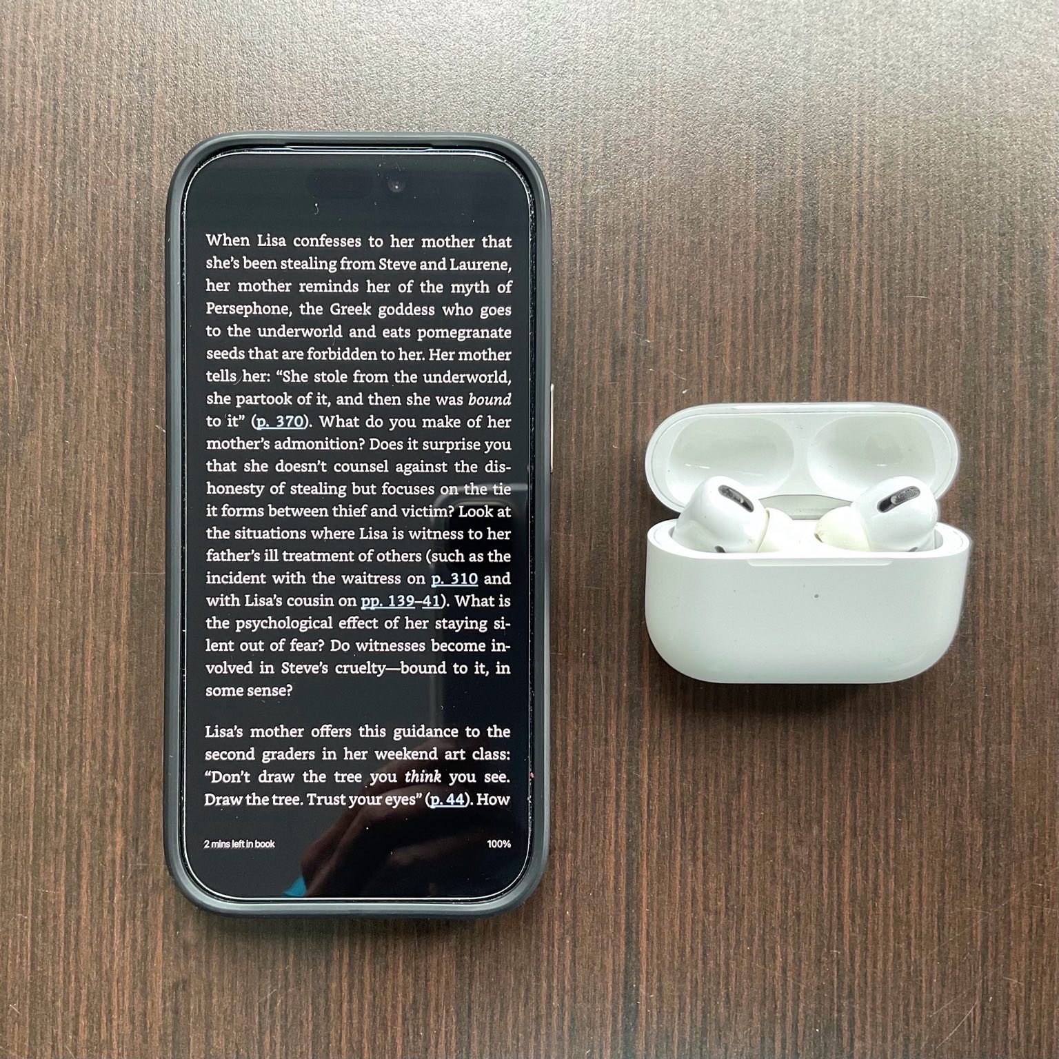 A page from Lisa Brennan-Jobs' "Small Fry" book in the Kindle app on an iPhone 17 Pro next to Apple AirPods Pro earbuds and case.