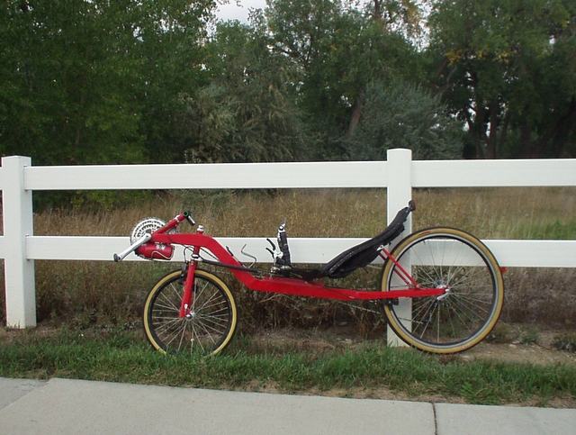 red Reynolds Wishbone recumbent against a white fence.