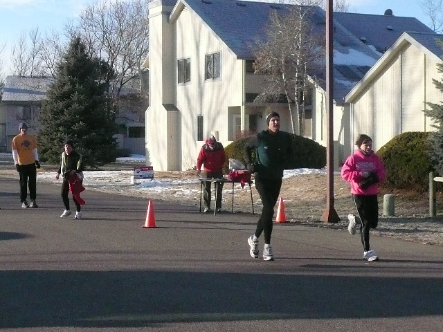 four runners running past orange cones and an apartment complex