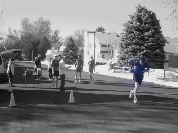 black and white photo of a half dozen runners near race start, with a man wearing a blue shirt starting next to two cones