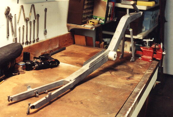 unpainted Reynolds Wishbone recumbent frame on a workbench, rear view