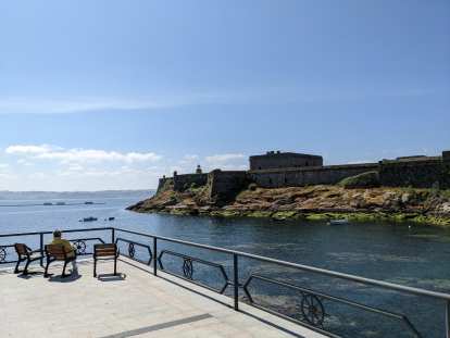 A man reading in a chair with a view of the Castle of San Antón.