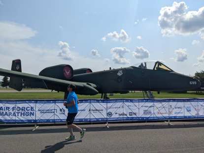 A marathoner runs by a rescue plane in the 2022 Air Force Marathon.