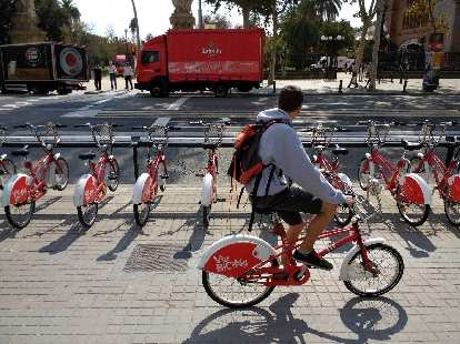A commuter biking past the row of red and white Bicing city share bicycles.