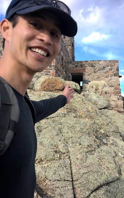 Felix Wong and a mountain goat at the stone lookout tower at the top of Harney Peak.