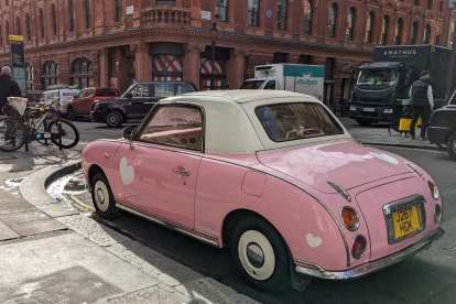 A pink Nissan Figaro with a white convertible top.