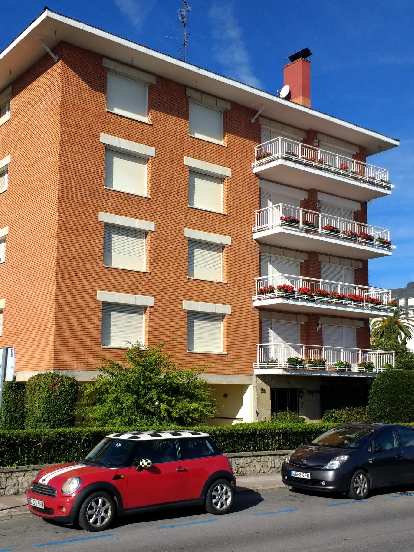 A red Mini Cooper coupe with white racing stripes and white and black roof in front of an orange four-story building. (27 Sep 2017) A red Mini Cooper coupe with white racing stripes and white and black roof in front of an orange four-story building.