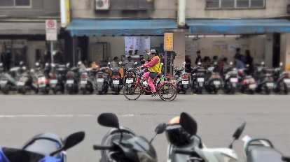 Man in pink pedaling a pink tricycle among a sea of motorbikes in Taipei, Taiwan.