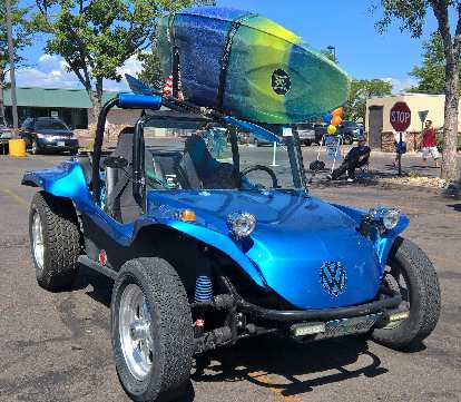 A blue Volkswagen dune buggy with a surfboard on top.
