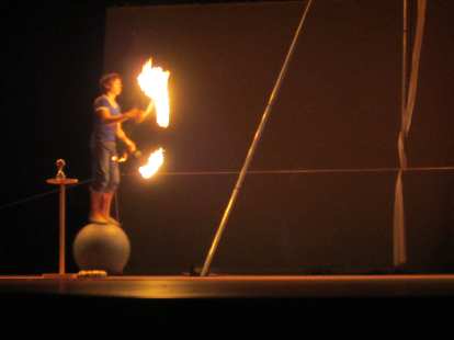 Sven Jorgensen juggling some fire sticks while rolling on top of a ball.