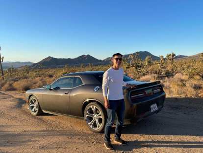 Felix Wong with a hand on a grey Dodge Challenger R/T in the Arizona desert.