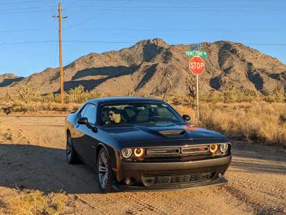 Right front three-quarter view of a dark grey Dodge Challenger R/T in the Arizona desert, with Andrea inside.