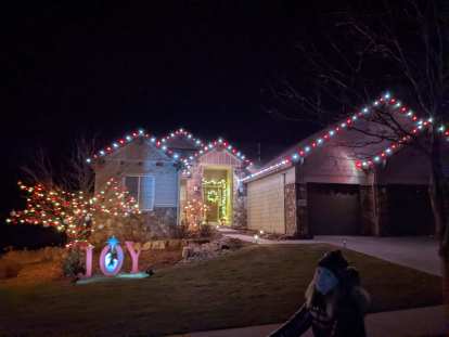 Andrea bikes by a house that is lit by Christmas lights and has the illuminated word JOY on the lawn.