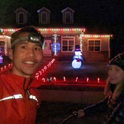 Felix and Andrea in front of a house lit by Christmas lights and an illuminated plastic snowman on the front lawn.