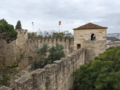 Two people peeking out of a window to take photos at the St. George Castle, with flags flying overhead.