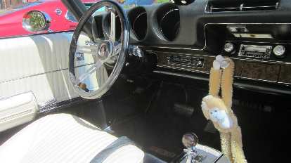 The interior of Oldsmobile 442 convertible with a monkey hanging off a knob. white interior of Oldsmobile 442 convertible, monkey hanging off knob