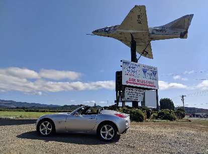 Silver Pontiac Solstice GXP in front of a Navy jet at the Tillamook Air Museum.