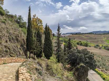 View of a stone path leading down to fields with the white houses of Ronda in the background.