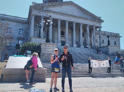 Mel Sirois and Felix Wong with their first-place age-group trophies at the 2020 Run Hard Columbia Marathon in front of the state capital.