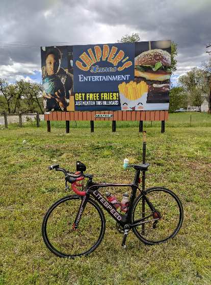 Mile 101: "Get free fries!" My black Litespeed Archon C2 in front of a billboard for Chipper's Lanes in Loveland, Colorado.