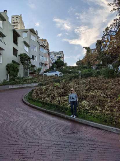 Andrea standing on a curb by the cobble stones of the most famous stretch of Lombard Street in San Francisco.