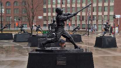 Felix Wong peaks his head between the legs of a baseball player statue at Busch Stadium. baseball player statues, Busch Stadium, Felix Wong's head