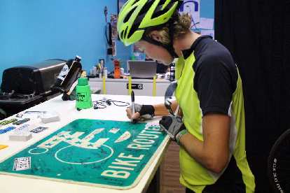 Jill Stetter signing a Bike Route sign at Newton Bike Shop in Newton, Kansas.