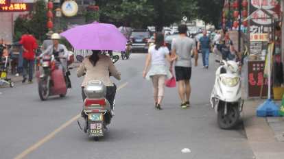 Woman driving a motorbike with a fixed purple umbrella in an area near Tunxi Ancient Street of Huangshan City. (20 May 2014) Woman driving a motorbike with a fixed purple umbrella in an area near Tunxi Ancient Street of Huangshan City.