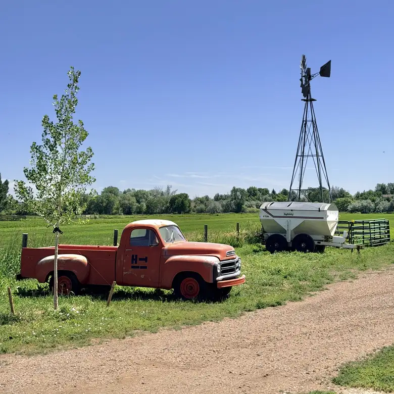 An orange International Harvester pickup truck from the 1950s alongside a windmill and a trailer. An orange International Harvester pickup truck from the 1950s alongside a windmill and a trailer.