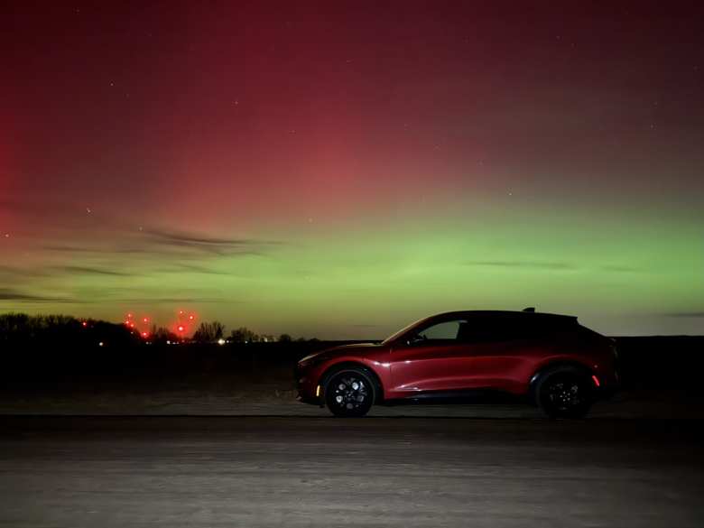The aurora over my Mustang Mach-E. The red lights at the left are from the NIST radio towers that broadcast time code signals from the nation's atomic clock to most of North America.