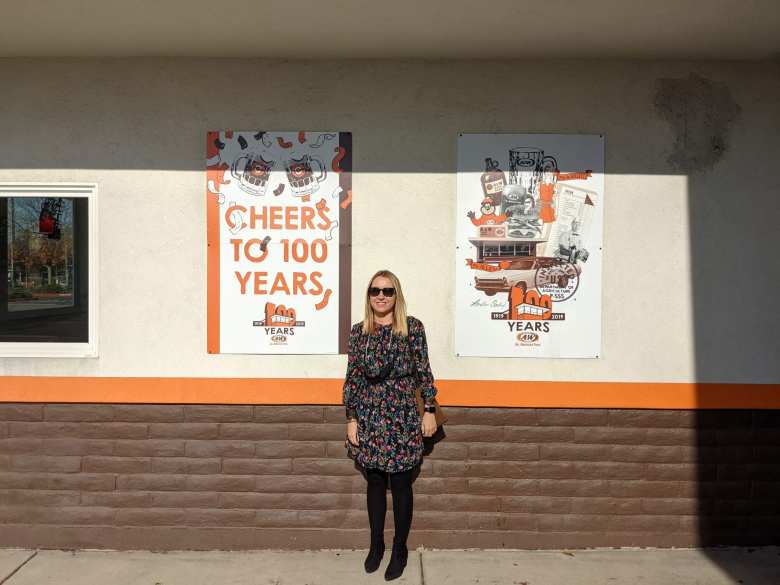 Andrea standing next to a sign saying "Cheers to 100 years (1919-2019)".