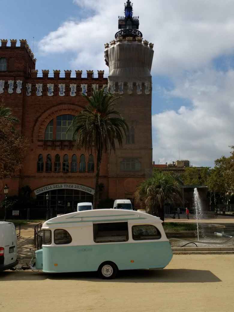 A teal and white trailer in front of a fountain and the Castell de Tres Dragons at the Parc de la Ciutadella in Barcelona, Spain.