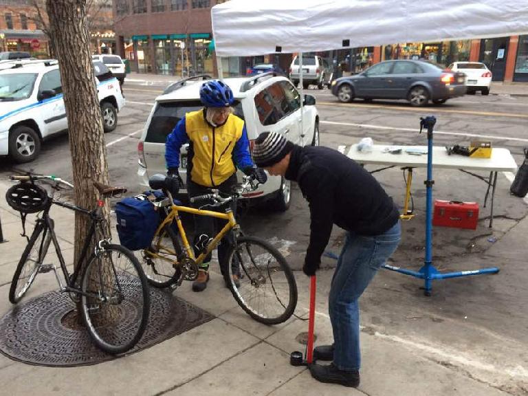 Felix Wong pumping up a commuter's front bicycle tire during Fort Collins Winter Bike to Work Day.