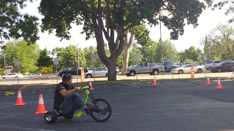 Riding a tricycle around a parking lot course at a Fort Collins Bike to Work Day station off Meldrum and Oak Street.